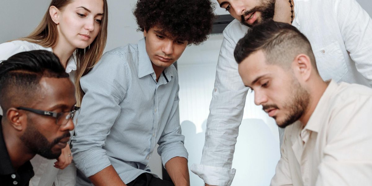 A diverse team of professionals actively collaborating around a large table in a modern, bustling office environment.